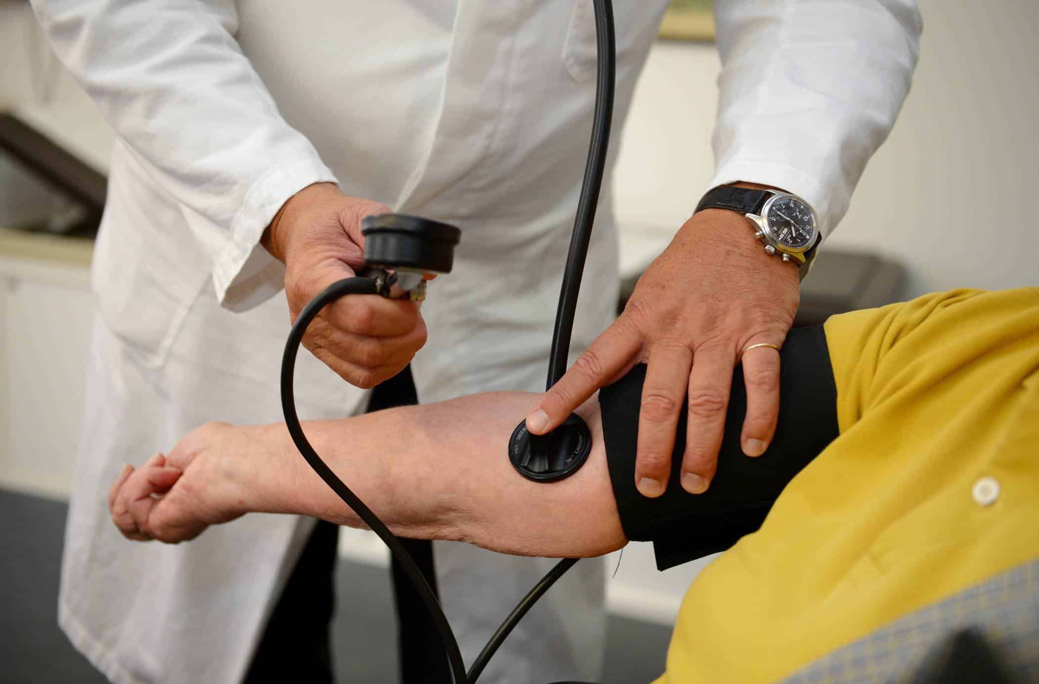 Ein Arzt misst den Blutdruck eines Patienten mit einem Blutdruckmessgerät am Arm des Patienten.