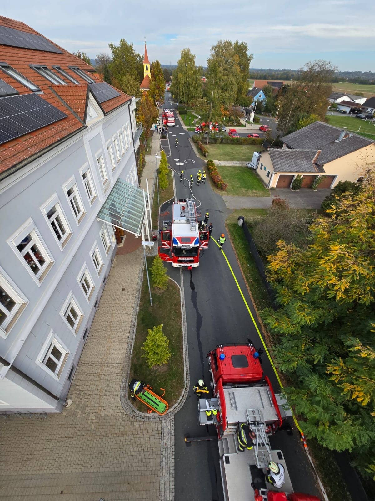 Feuerwehrleute und Rettungsfahrzeuge auf einer Straße vor einem Gebäude, daneben steht eine Rettungstrage auf dem Boden.
